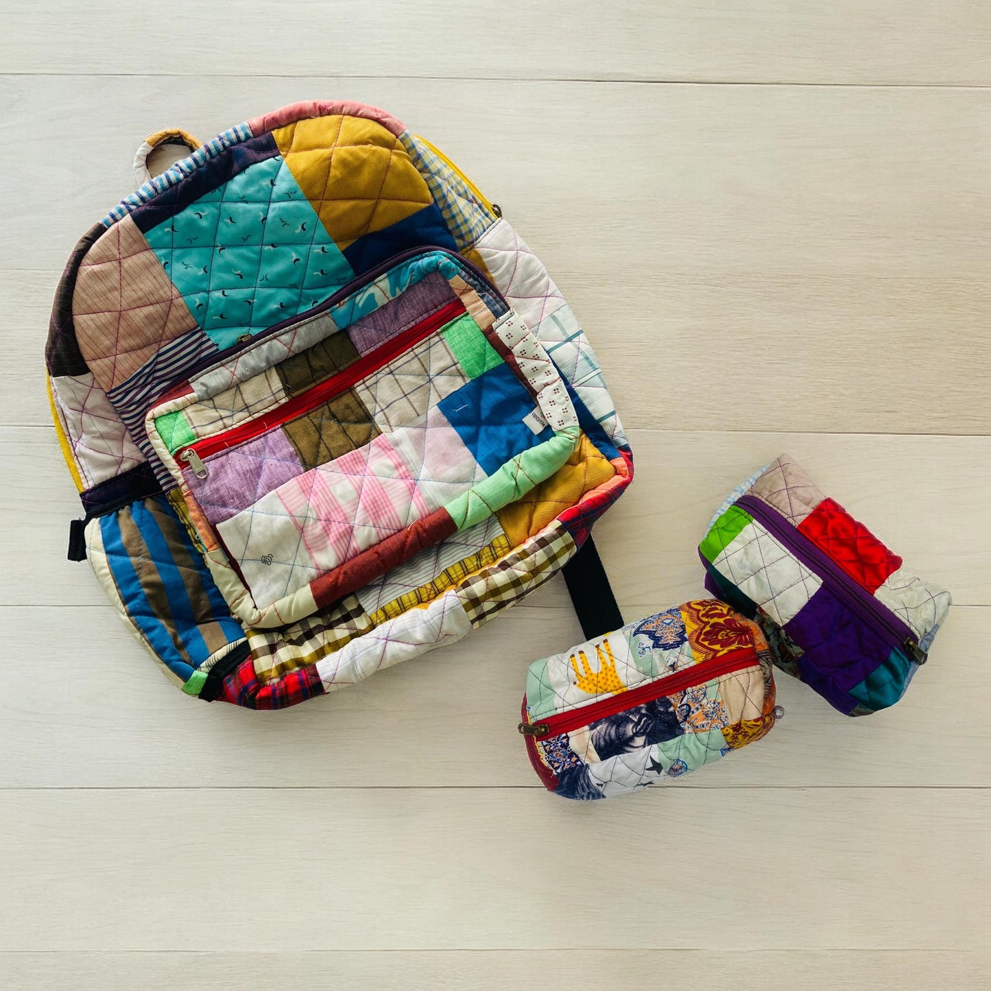 Eco-friendly patchwork backpack and two colorful quilted pouches laid out on a clean wood surface. Each piece is handmade using rescued fabric scraps, making them one-of-a-kind. The set is ideal for travel, toddler backpacks, baby shower gifts, school essentials, and daily organization. A thoughtful, sustainable choice for eco-conscious users looking for stylish, functional storage options.