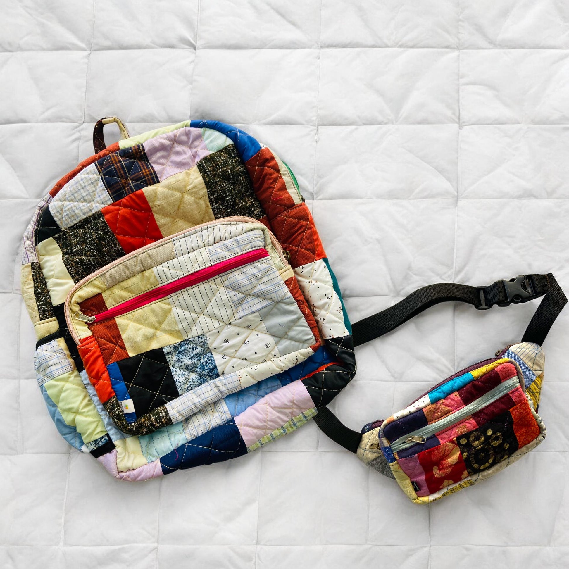 Handcrafted eco-friendly patchwork backpack with matching fanny pack laid on a white quilted background. Both items are made from upcycled cotton fabrics in bright, colorful patterns. Ideal for travel, school, and outdoor adventures. Sustainable and stylish, this set is perfect for women, kids, and eco-conscious buyers looking for functional and unique accessories with a handmade charm.