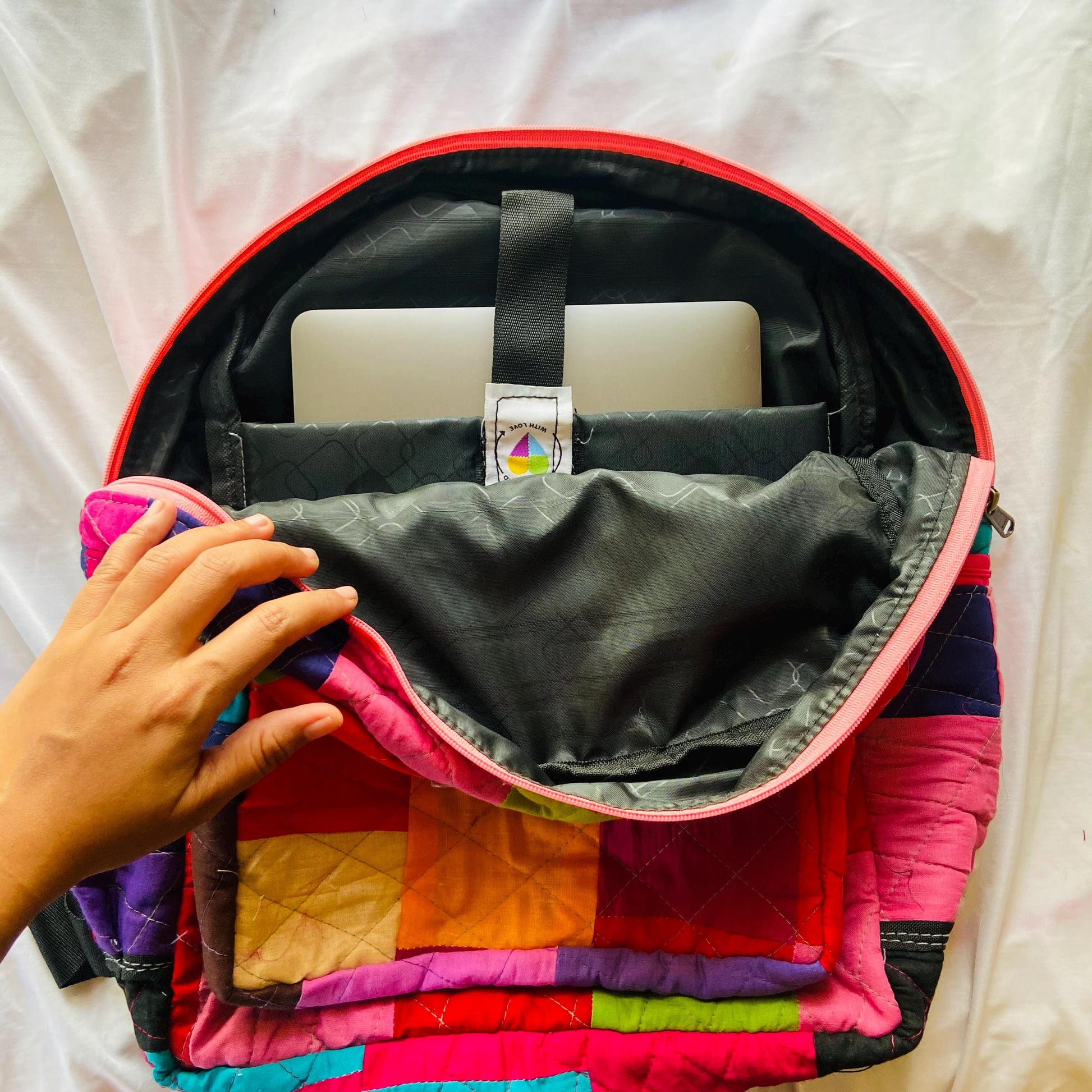 Backpack and padded laptop sleeve placed on a wooden floor. The MacBook is partially inserted into the sleeve, highlighting its snug fit and functional use. Both accessories feature eco-friendly, handmade patchwork crafted from upcycled cotton fabric. Ideal for gifting, school, or remote work. A sustainable, zero-waste solution for creative users who love bold, colorful designs. This image showcases the laptop in the open backpack