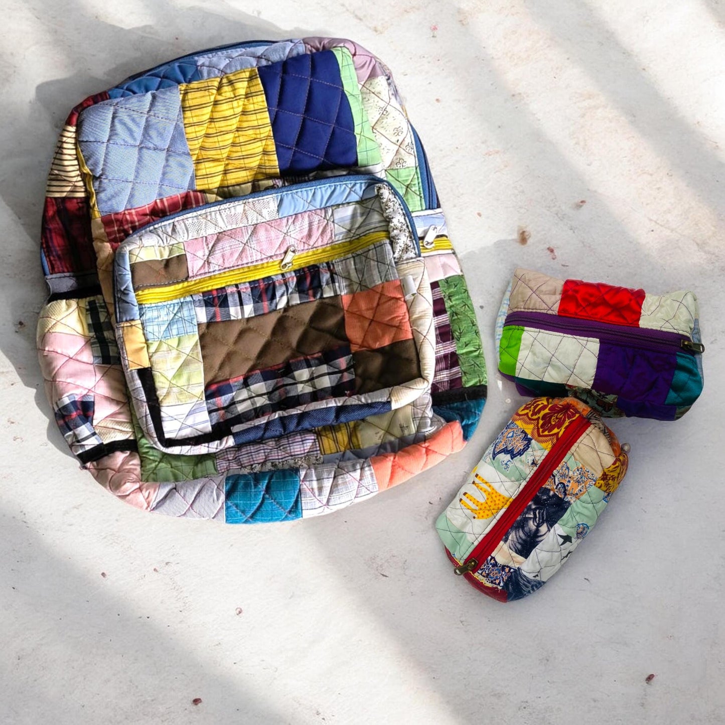 Patchwork backpack with dual matching pouches placed on a sunlit white surface. Handmade using colorful rescued textile pieces with quilted texture and vibrant zippers. Ideal for travel, school, gifting, and daily adventures. A thoughtful baby shower gift or eco home essential. These zero-waste bags are functional, lightweight, and designed for sustainable, conscious living and joyful organization.