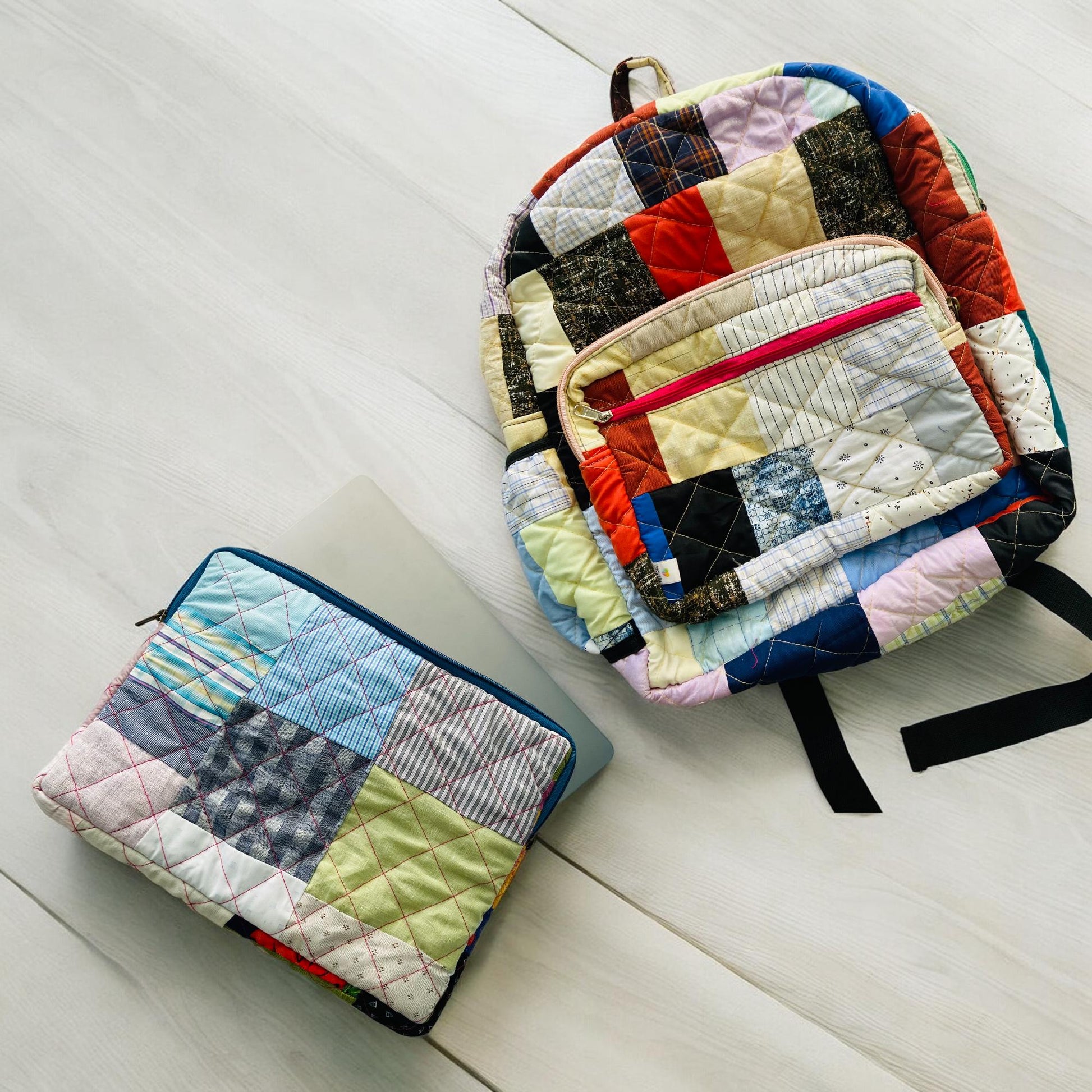 Backpack and padded laptop sleeve placed on a wooden floor. The MacBook is partially inserted into the sleeve, highlighting its snug fit and functional use. Both accessories feature eco-friendly, handmade patchwork crafted from upcycled cotton fabric. Ideal for gifting, school, or remote work. A sustainable, zero-waste solution for creative users who love bold, colorful designs.