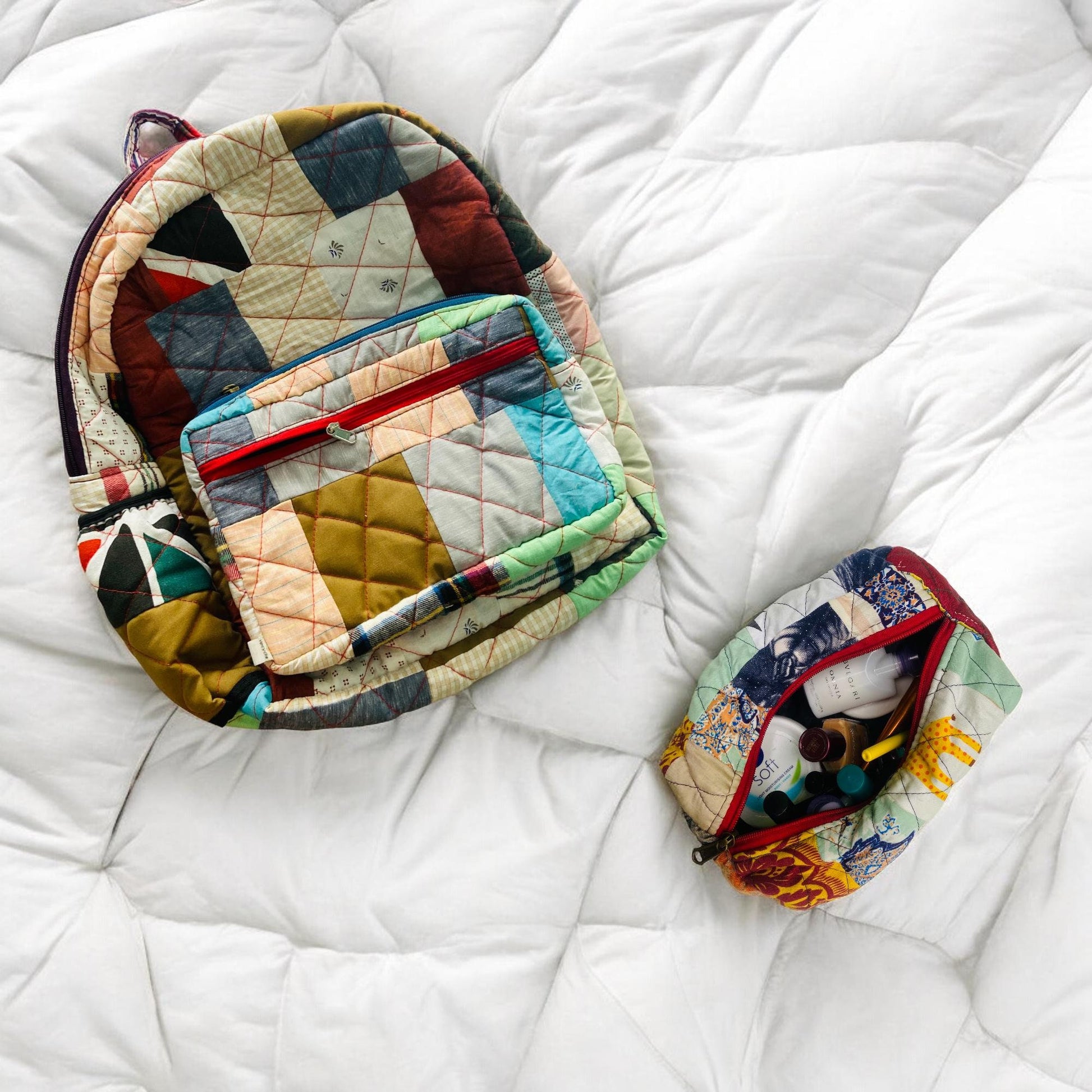 Trendy eco-friendly patchwork backpack and matching quilted pouch displayed on a soft white comforter. The backpack features vibrant fabric blends with a red zipper, while the pouch is filled with essentials. Ideal for travel, school, and daily use. Stylish backpack gift for women, girls, and toddlers. Great baby shower gift or back-to-school option made using sustainable methods from rescued textile extras.