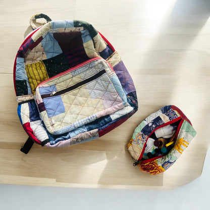 Flat-lay image of a patchwork backpack and pouch set on a light wood surface. Backpack features a large zippered pocket, while the pouch contains small toiletry items. Eco-friendly, upcycled, and quilted, the set is ideal for school, toddler backpacks, gifting, and beach travel. A versatile handmade backpack set for women, boys, and girls with a love for colorful, sustainable lifestyle accessories.
