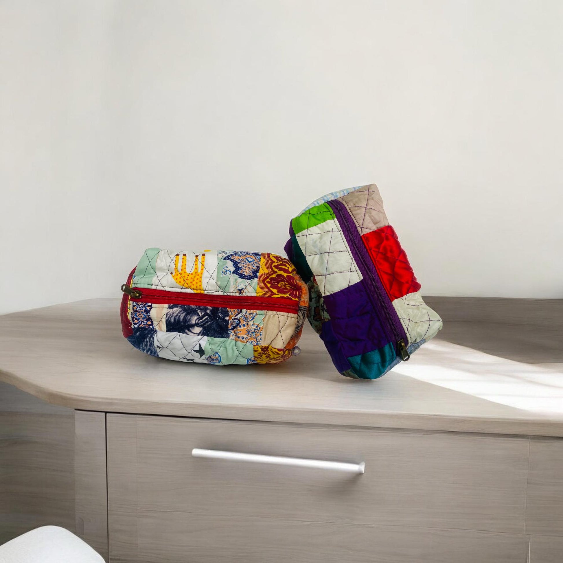Two compact quilted pouches made from upcycled fabrics sitting on a wooden cabinet under soft sunlight. These sustainable bags feature vibrant patchwork and bold zippers, making them perfect for travel organization, eco home storage, or school supplies. Great as a handmade gift for women, kids, and eco warriors. Lightweight, durable, and ideal for a zero-waste, plastic-free lifestyle.
