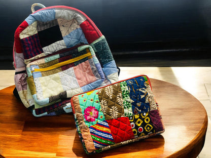 Handmade eco-friendly patchwork backpack and laptop sleeve placed on a polished wooden surface. Both are quilted using vibrant fabric remnants, showcasing traditional and tribal motifs. This sustainable set is perfect for travel, school, or gifting. Ideal for women, students, and eco-conscious users who want to stay stylish while reducing textile waste with practical upcycled accessories.