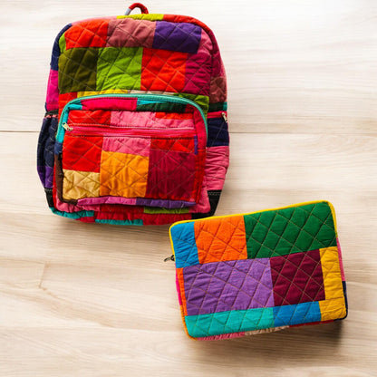 Backpack and padded laptop sleeve placed on a wooden floor. The MacBook is partially inserted into the sleeve, highlighting its snug fit and functional use. Both accessories feature eco-friendly, handmade patchwork crafted from upcycled cotton fabric. Ideal for gifting, school, or remote work. A sustainable, zero-waste solution for creative users who love bold, colorful designs. this image shows the multicolor solids all colorful laptop sleeve and backpack