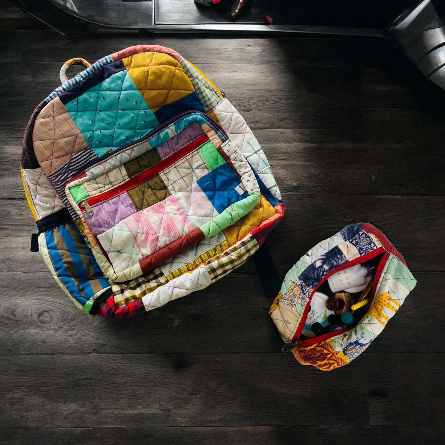 Colorful patchwork backpack made from upcycled fabric scraps, shown on a wooden floor with a matching pouch beside it filled with travel-size toiletries. The eco-friendly backpack features a quilted design, bright red zipper, and sustainable style perfect for travel, beach trips, or gifting. Ideal for women, kids, and eco-conscious buyers looking for unique handmade bags and accessories.