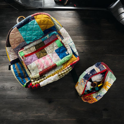 Colorful patchwork backpack made from upcycled fabric scraps, shown on a wooden floor with a matching pouch beside it filled with travel-size toiletries. The eco-friendly backpack features a quilted design, bright red zipper, and sustainable style perfect for travel, beach trips, or gifting. Ideal for women, kids, and eco-conscious buyers looking for unique handmade bags and accessories.