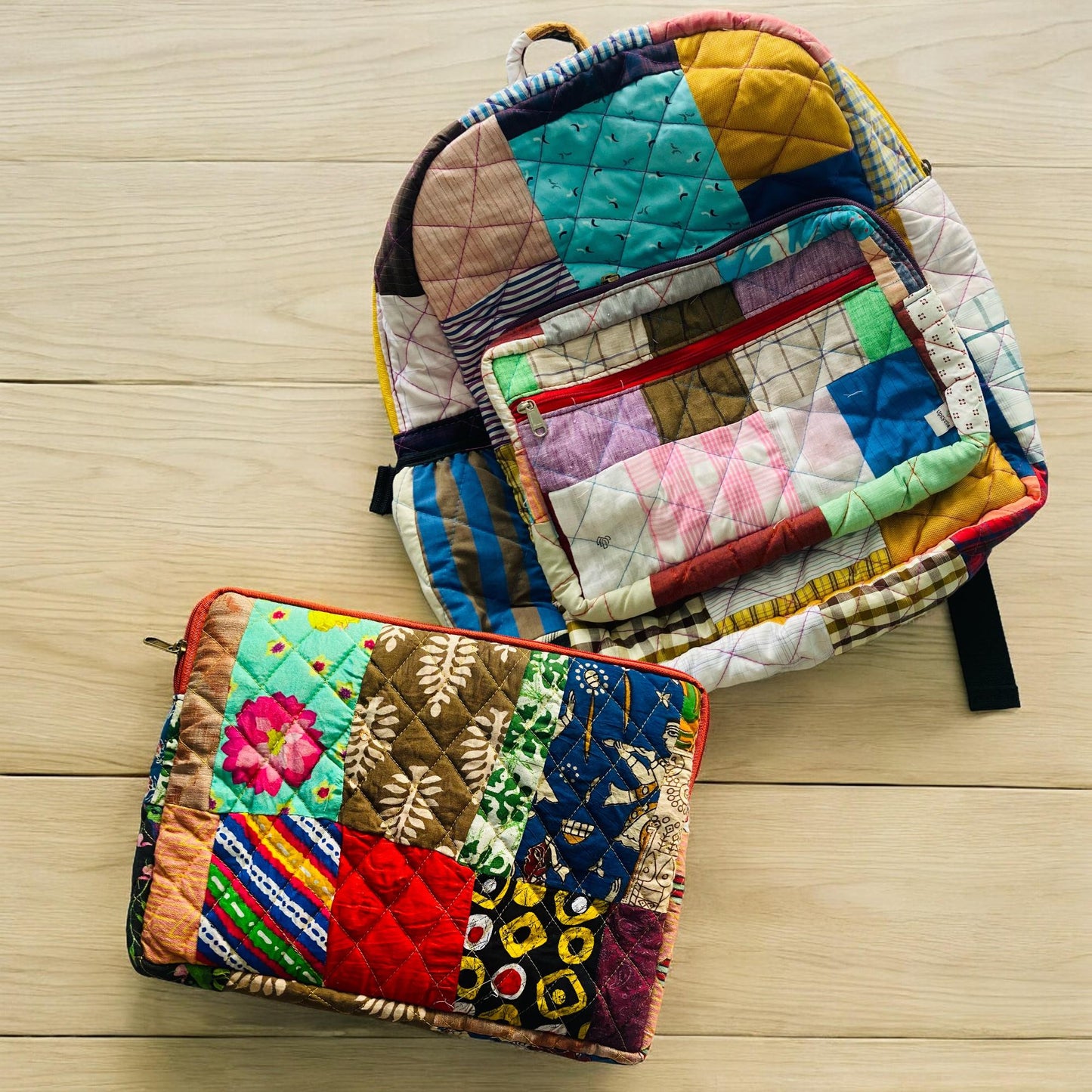 Colorful handmade backpack and laptop sleeve with vivid patchwork featuring florals, tribal prints, and geometric patterns. Shown on a light wooden floor, this set is crafted using rescued textile scraps, promoting a zero-waste lifestyle. Ideal for eco-conscious students, creatives, or professionals who need functional yet expressive accessories for school, travel, or daily errands.